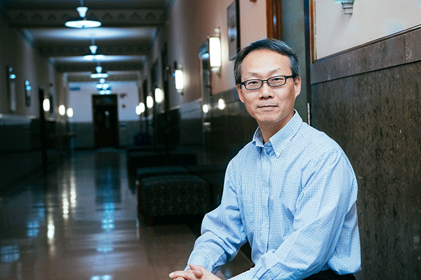 Male professor looking into the camera on the left side of the image with a hallway visible on the right.  